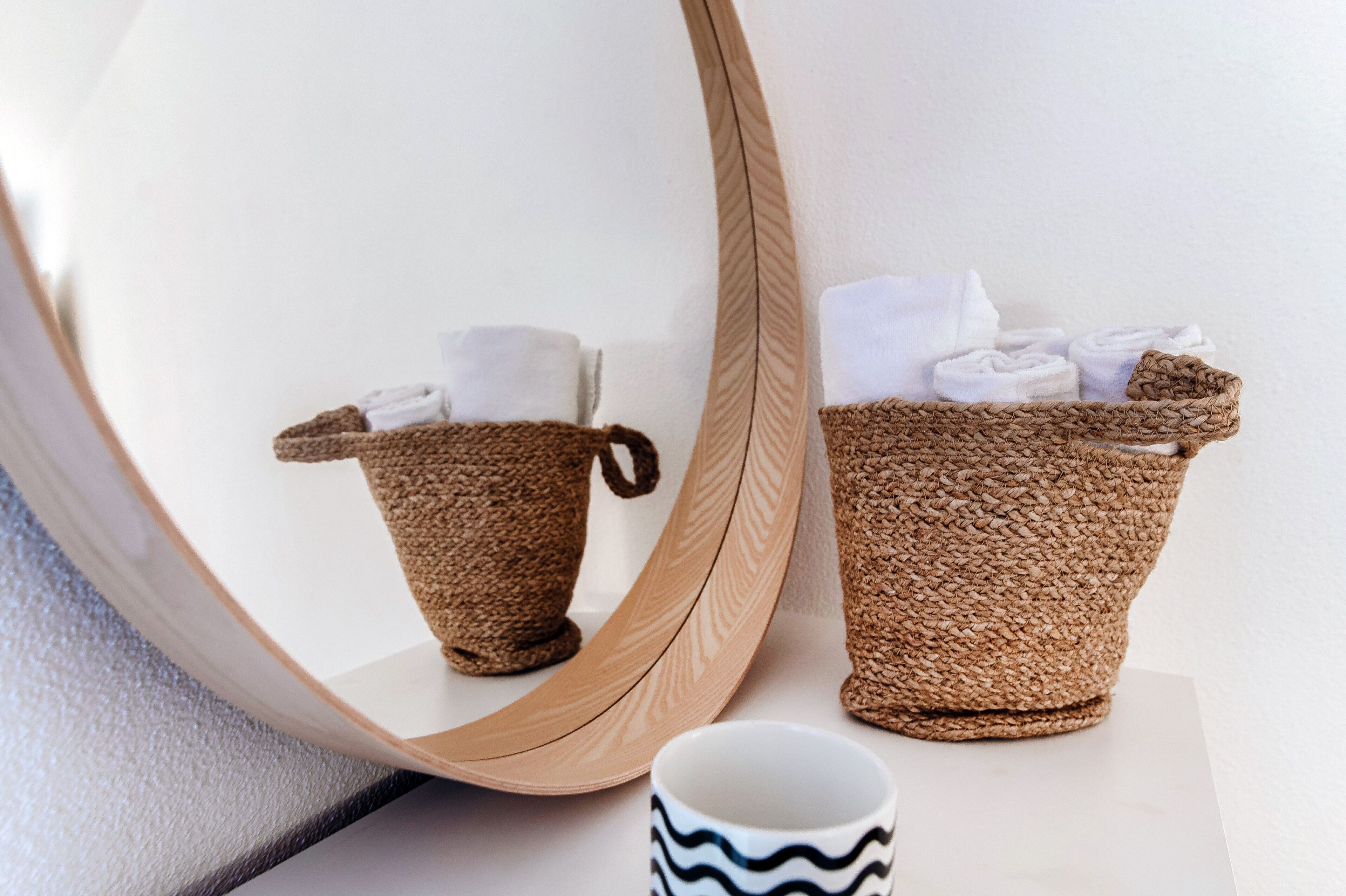 Un miroir reflète un panier tressé contenant des serviettes et une tasse.