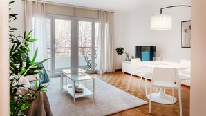 A modern living room with a glass coffee table, white sofa, and a dining area with a white table and chairs. - Pink Flat  (Chiasso)