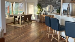 A modern kitchen with a stone backsplash, wooden flooring, and a dining area with a large table and chairs. - Stylish Lake Retreat on Blue Bay, Flathead Lake, Montana with private beach! (Polson)