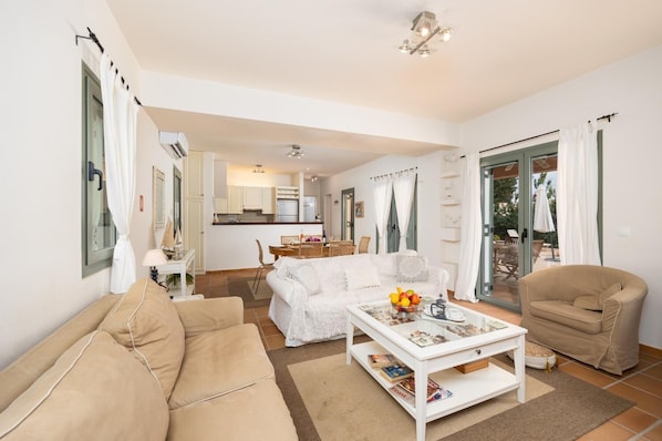 Ein modernes Wohnzimmer mit Sofa, Sessel, Couchtisch und einem Essbereich im Hintergrund.