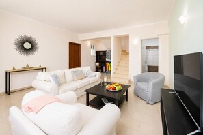 Una sala de estar con un sofá, una mesa de centro con fruta, un televisor y una escalera que lleva a otra habitación.