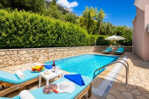 Un área de piscina con sillones, una mesa con comida y bebidas, y una pared de piedra.