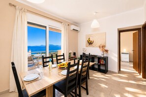 Un coin repas avec vue sur la mer, une table dressée avec des assiettes et des verres à vin, et une bibliothèque contenant des livres et des objets décoratifs.