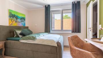 A bedroom with a bed, a chair, a painting, and a window with curtains.