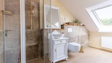 A bathroom with a glass-enclosed shower, a white vanity with a large mirror, and a window providing natural light.