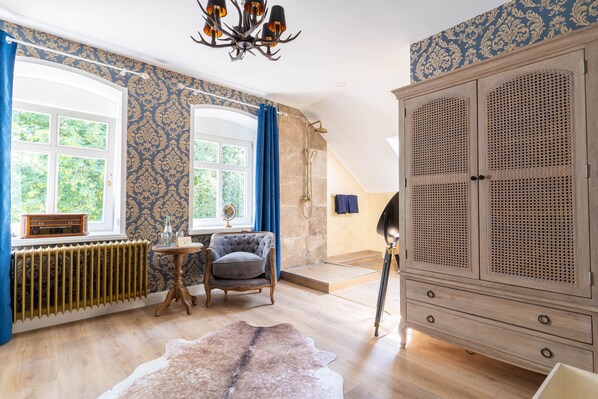A room with a large wooden wardrobe, a classic armchair, a radiator, and a patterned wallpaper.