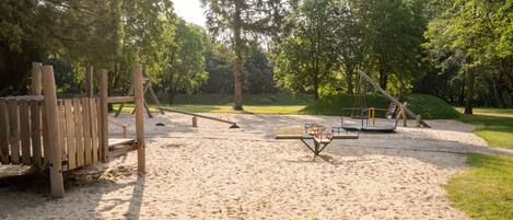 Un parque infantil con arena, estructuras de madera y columpios.