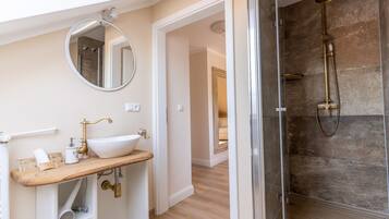 A bathroom with a wooden vanity, a white sink, a round mirror, and a glass-enclosed shower area.