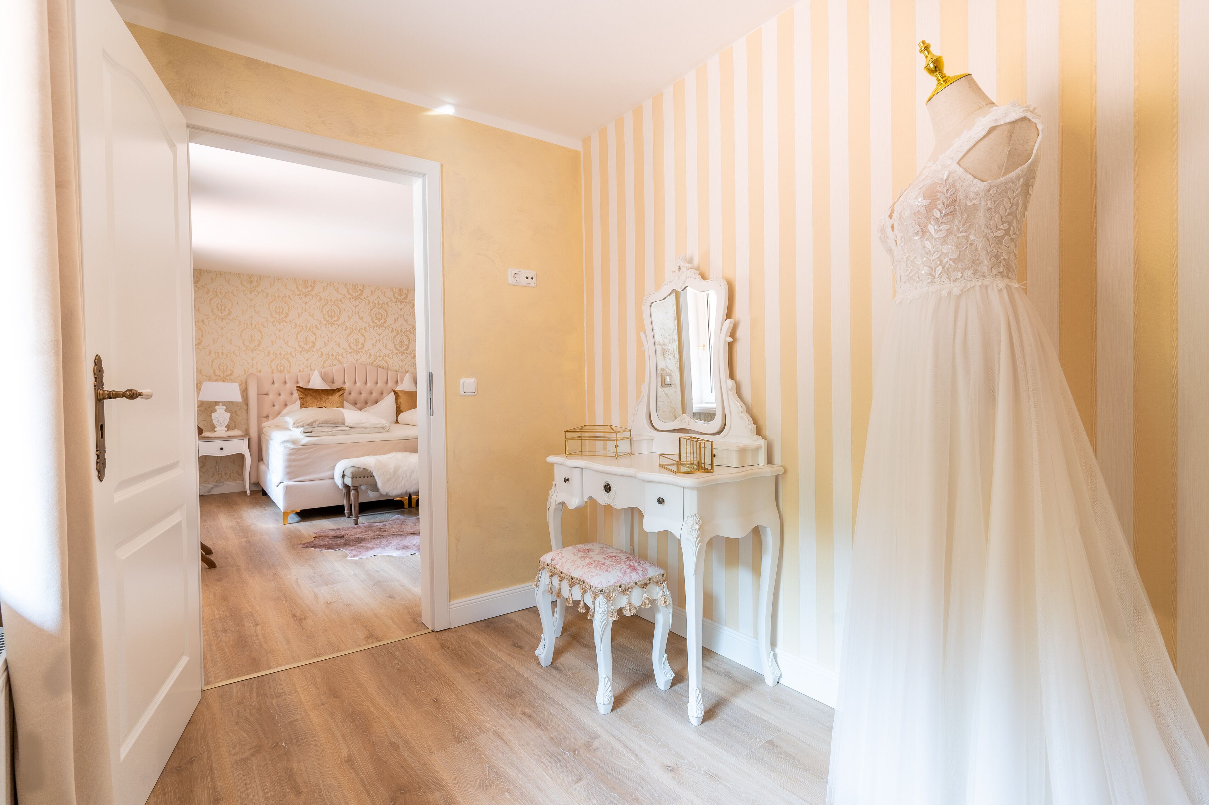 A room with a bed, a vanity with a mirror, and a dress on a mannequin.