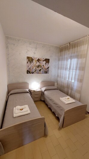 Une chambre avec deux lits, une table de chevet, un tableau et une fenêtre avec des rideaux.