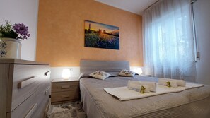 Une chambre à coucher avec un lit, des tables de chevet, une commode, un secrétaire, un tableau au mur et une fenêtre avec des rideaux.