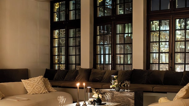 A modern living room with a beige sofa, a dark green ottoman, and a marble coffee table with candles. - Luxury Grand-Place Flat  (Brussels)