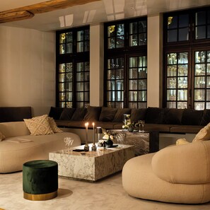 Un salon moderne avec un canapé beige, un pouf vert foncé et une table basse en marbre agrémentée de bougies.