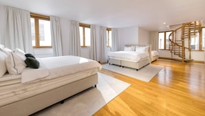 A spacious bedroom with two beds, wooden flooring, large windows with curtains, and a spiral staircase. - Luxury Grand-Place Flat  (Brussels)
