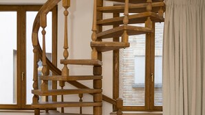 A wooden spiral staircase in a room with wooden flooring, a window with blinds, and a radiator. - Luxury Grand-Place Flat  (Brussels)
