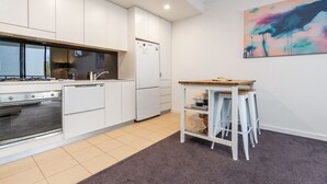 Ett modernt kök med vita skåp, en inbyggd ugn och en liten matplats med barstolar.