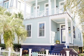 A light blue two-story house with white trim, a front porch, and a white picket fence. - Summer Special! Cute Cottage Steps to Beach & Pool (St. Simons Island)