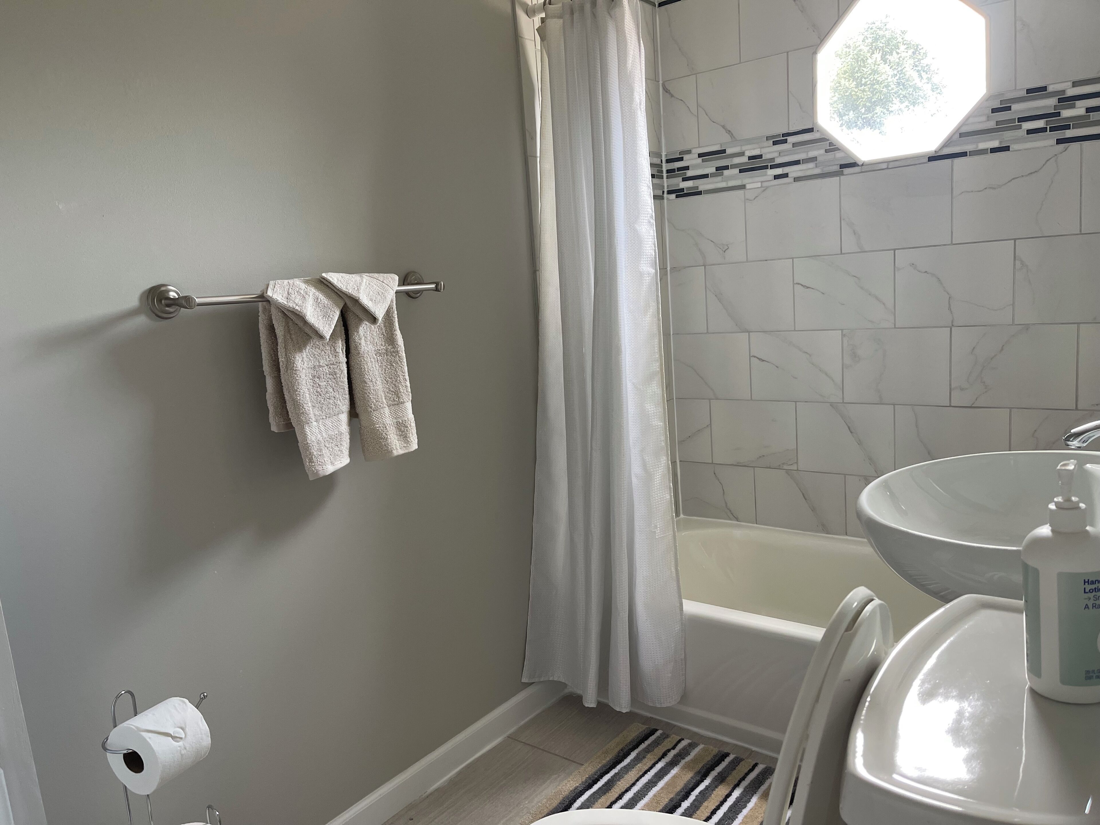 Une salle de bain avec une baignoire, un lavabo, un porte-serviettes avec des serviettes, un porte-rouleau de papier toilette et un tapis à rayures.