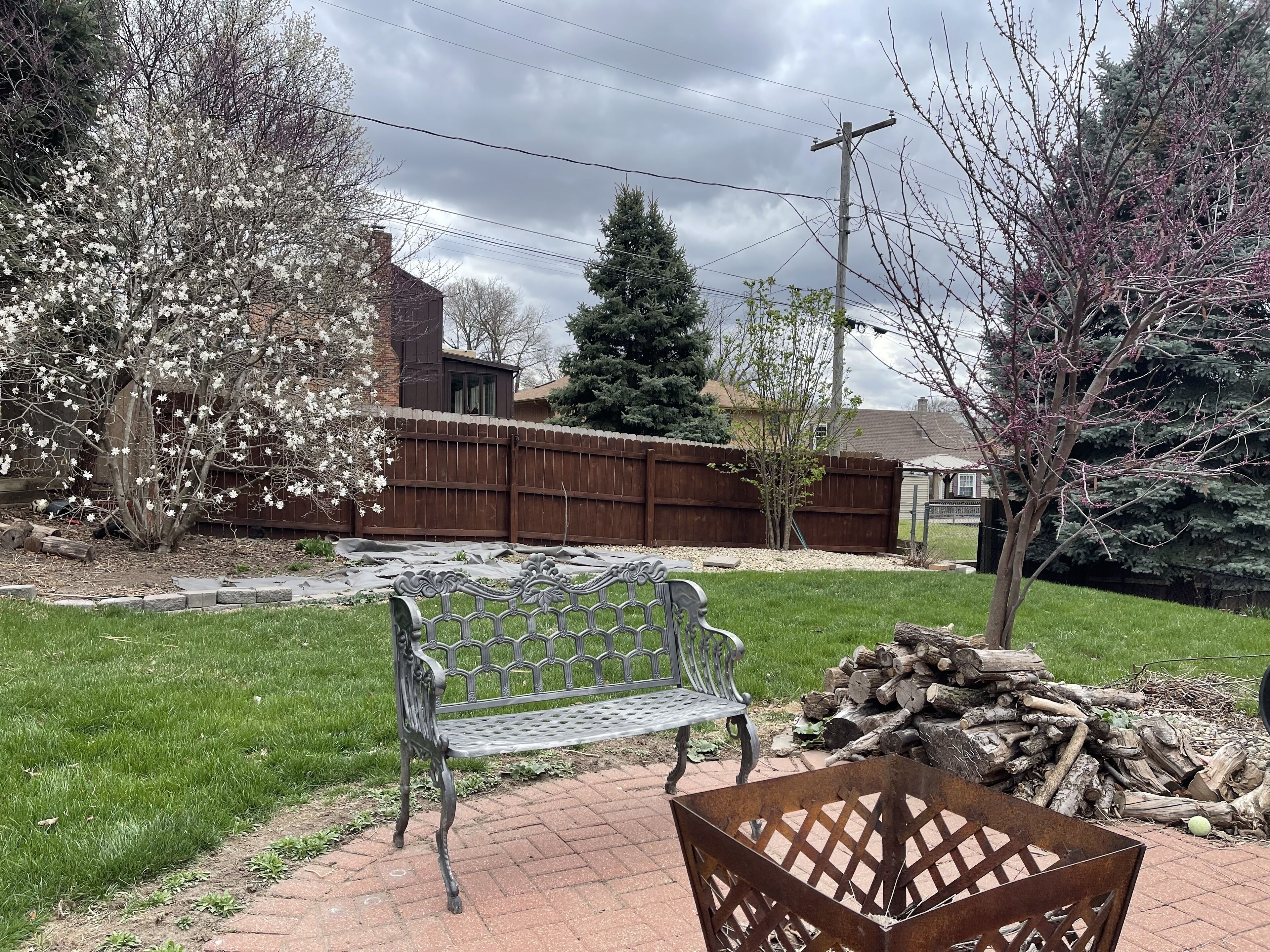 A backyard with a metal bench, a wooden planter, and a pile of logs.