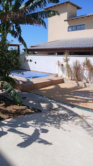 A patio area with a pool, surrounded by palm trees and a building with a tiled roof.
