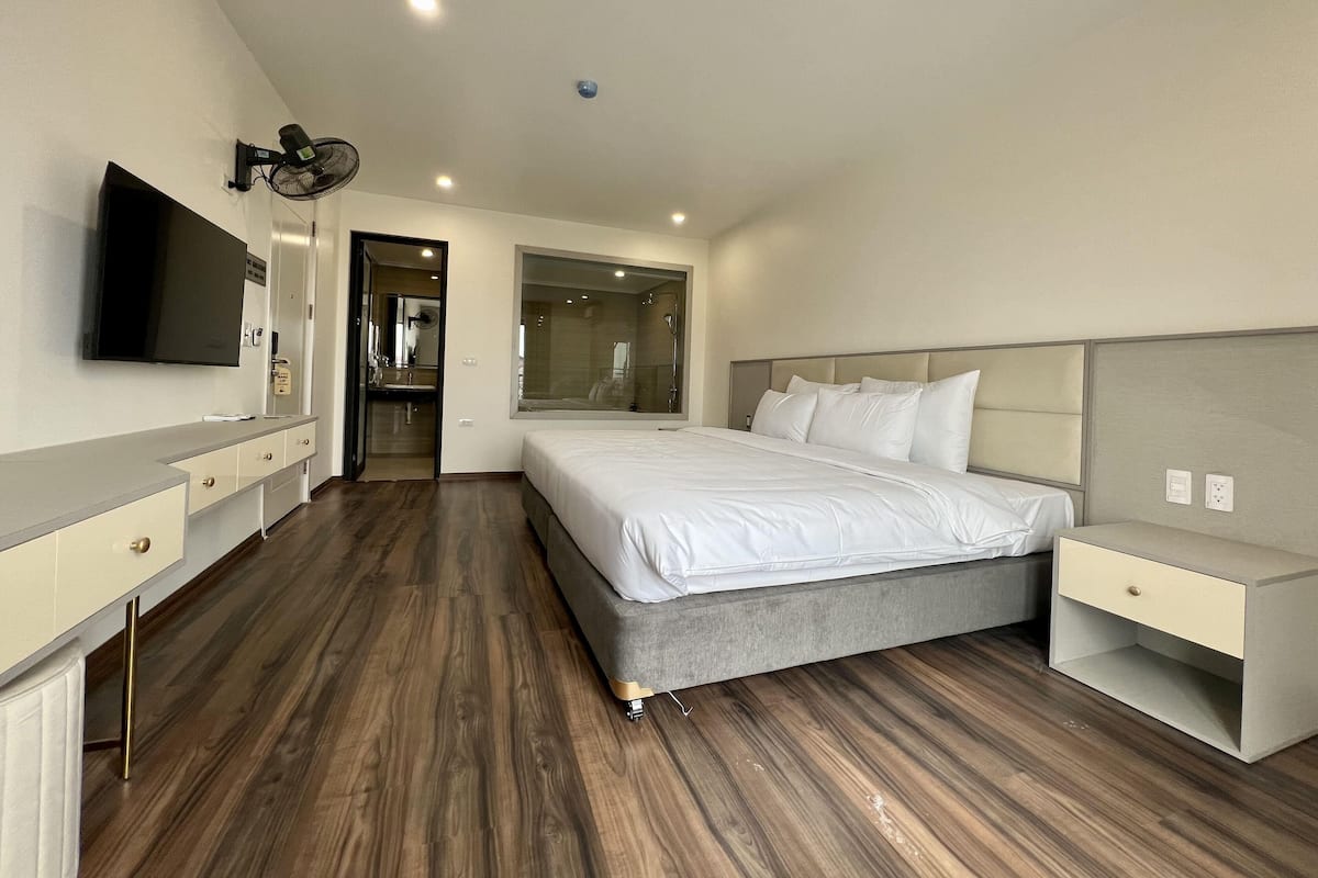 Una habitación de hotel moderna con una cama grande, mesitas de noche, un televisor y un baño visible a través de una puerta abierta.
