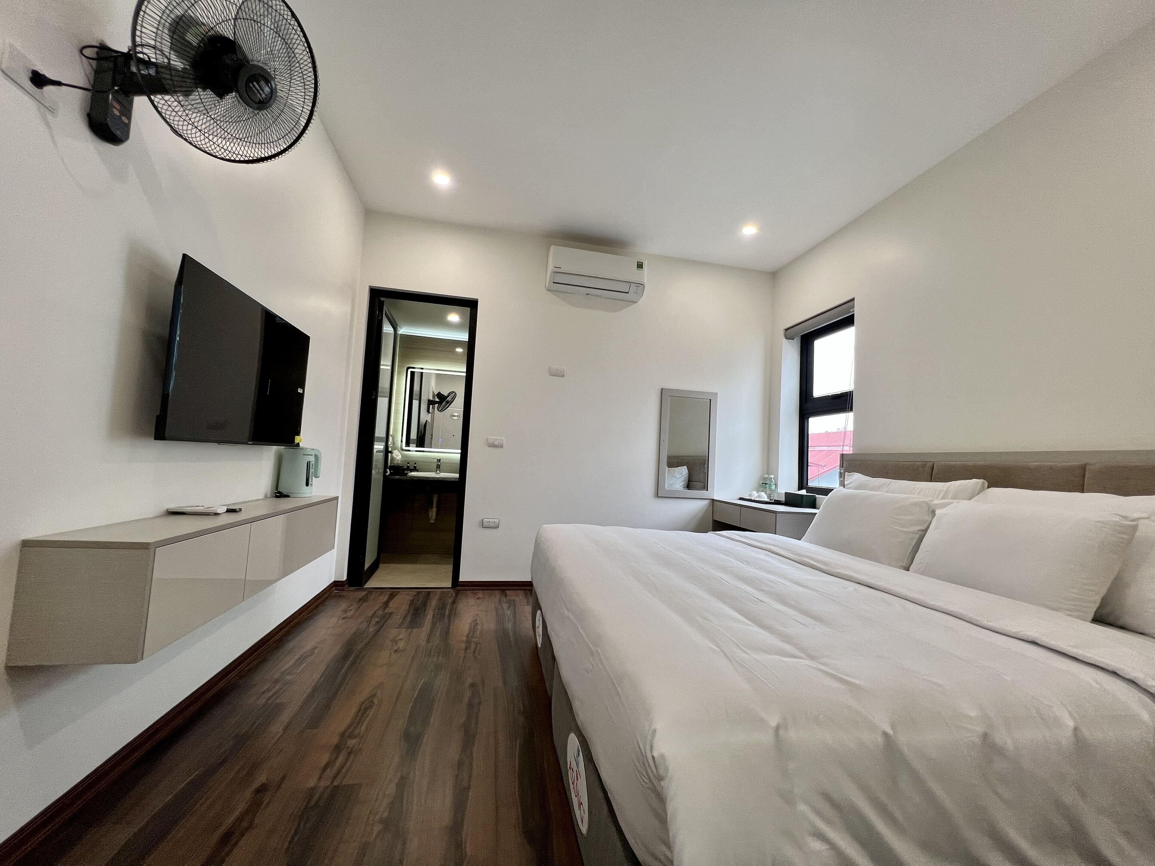 Een moderne hotelkamer met een groot bed, een aan de muur bevestigde televisie, een bureau met stoel, en een raam dat voor natuurlijk licht zorgt.