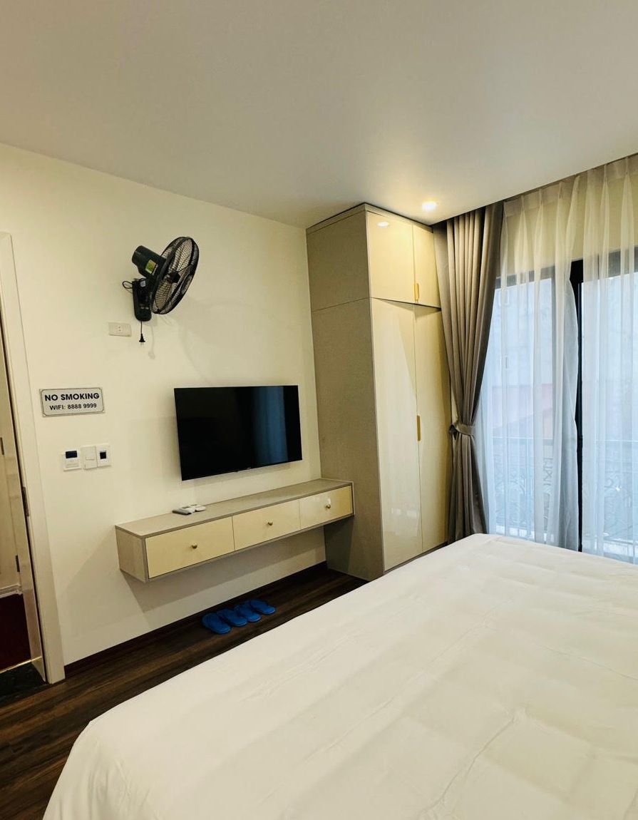 Et hotelværelse med en seng, et fjernsyn, en ventilator, et klædeskab og et skilt med røgforbud.