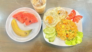 Une assiette de riz frit aux légumes et aux œufs, une assiette de pastèque et de bananes, et un verre de café glacé.