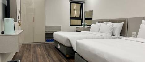 A hotel room with two beds, a desk, a mirror, and a wardrobe.