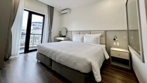 Une chambre d’hôtel moderne avec un grand lit, une table de chevet avec une lampe, un appareil de climatisation et une vue sur la ville depuis les portes du balcon.
