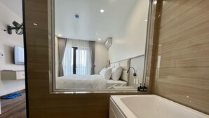 Une chambre d’hôtel moderne avec un grand miroir qui reflète le lit, une baignoire blanche et un téléviseur fixé au mur.