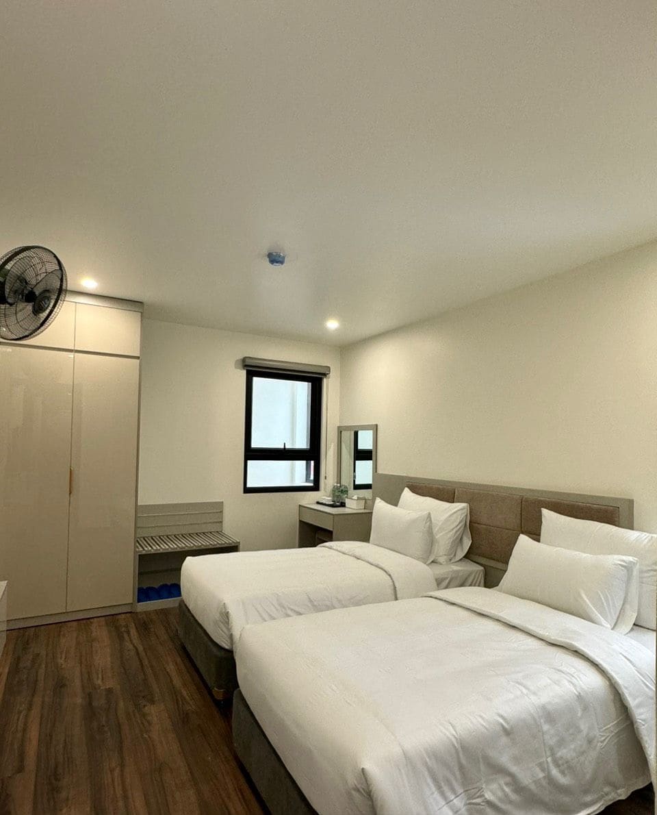 Habitación doble de lujo con dos camas, un armario, una mesita de noche, un espejo, una ventana y un ventilador de techo.
