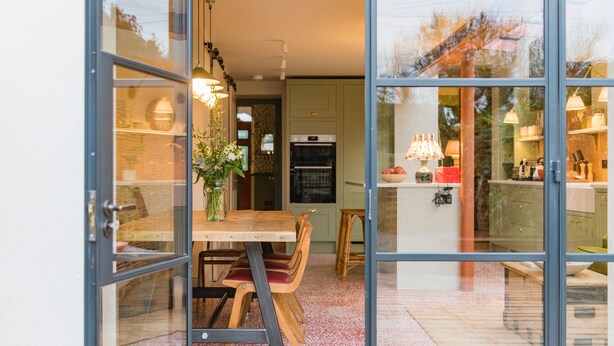 A modern kitchen with a dining area visible through glass doors.
