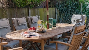 A wooden round table with chairs, a bottle of wine, a bowl of strawberries, and a magazine.
