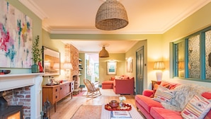 A cozy living room with a fireplace, a red sofa, and a dining area with a brick wall and wooden furniture.