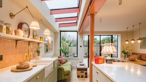 A modern kitchen with a skylight, a green sofa, and a dining area with a view of the garden.