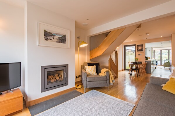 A modern living room with a fireplace, a television, and a dining area with natural light.