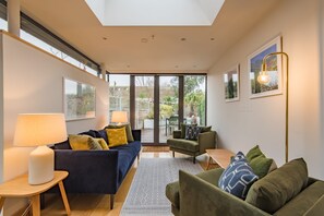 A modern living room with a sofa, armchairs, and a lamp. There is a large window and a door leading to an outdoor area. - Starboard Light, Whitstable (Whitstable)