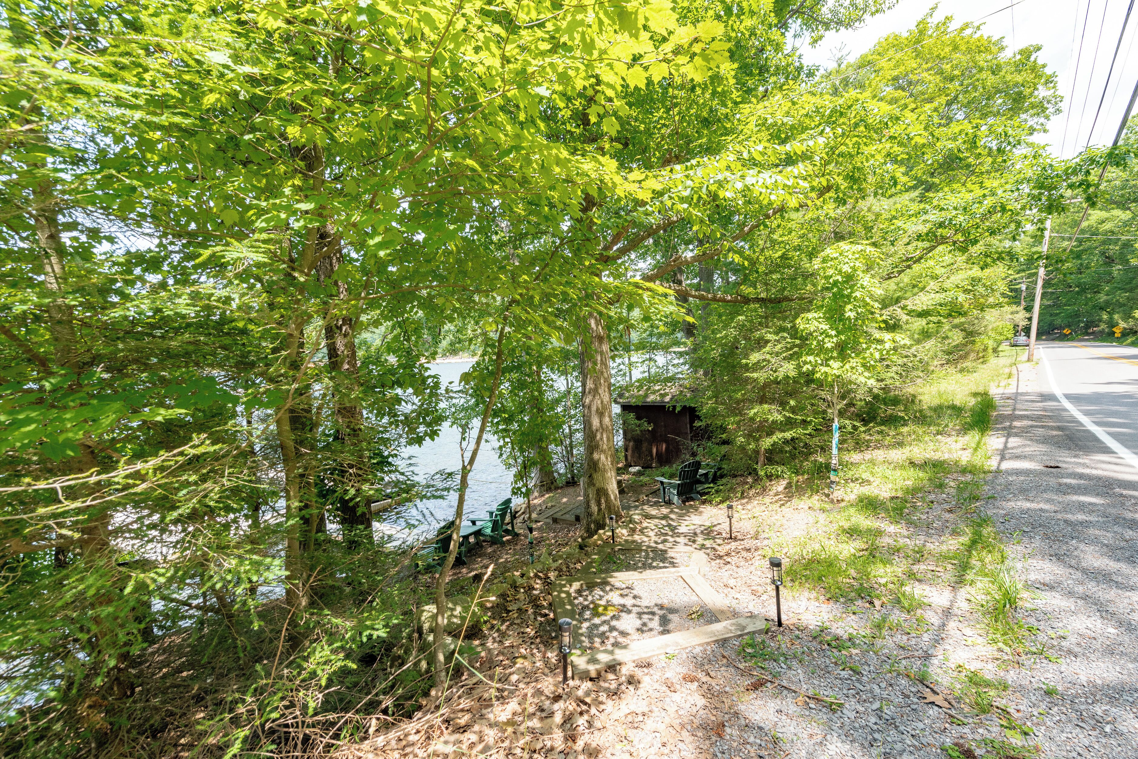 A pathway beside a lake with trees and a small wooden structure.