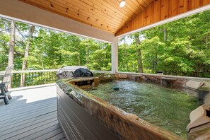 Un bain à remous sur une terrasse en bois, avec vue sur une forêt.