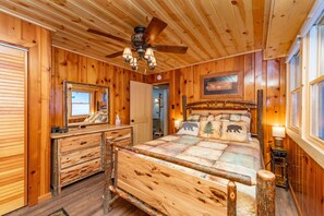 Une chambre dans une cabane en bois, avec un lit, une commode et un ventilateur de plafond.