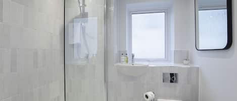 A modern bathroom with a glass shower enclosure, a toilet, a sink, and a window.