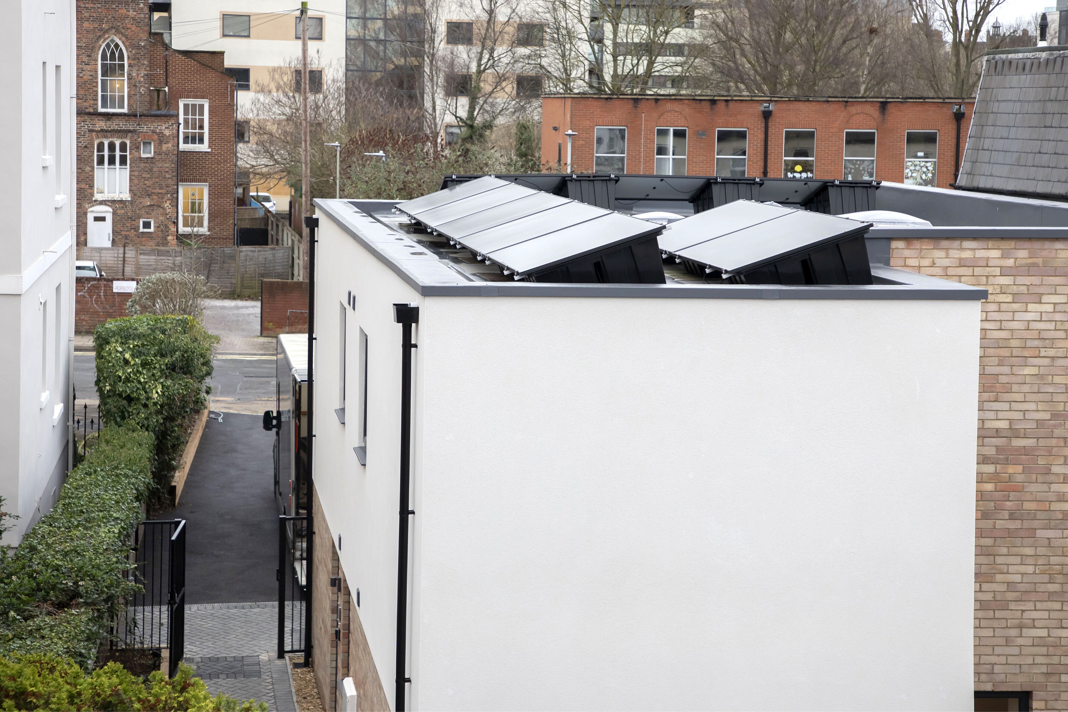 A building with a flat roof, solar panels, and a narrow alleyway.