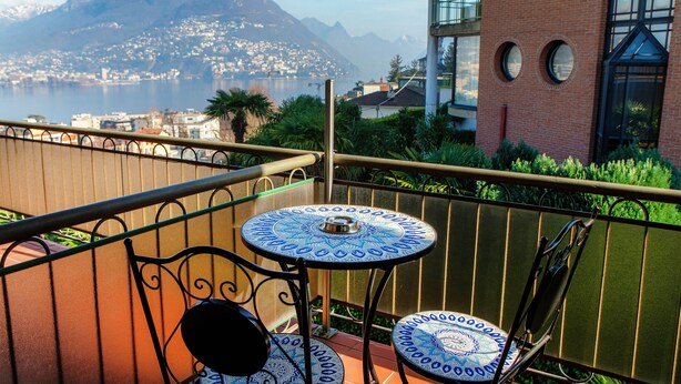 Un balcón con dos mesas y sillas con diseños, con vista a un paisaje montañoso y un cuerpo de agua.
