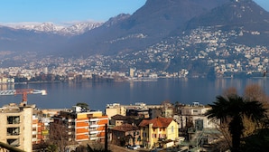 Un paisaje urbano costero con montañas al fondo, que muestra una combinación de edificios residenciales y comerciales, un puente destacado y una masa de agua tranquila.