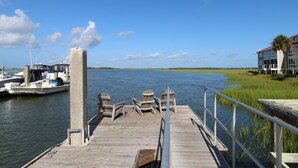 Une jetée en bois avec des chaises, un pilier en béton et, au fond, un bâtiment avec un toit rouge.