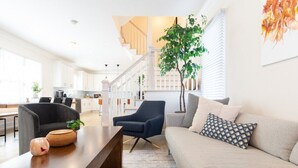 A modern living room with a sofa, a coffee table, and a chair. There is a staircase in the background leading to an upper floor. - Stay just a 3-minute walk from the beach in this stunning luxury home located between Ocean Grove & Asbury Park. Perfect for large families and groups, this spacious retreat offers modern amenities, multiple outdoor spaces, and everything you need. (Ocean Grove)