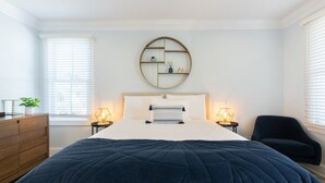 A bedroom with a large bed, a round wall shelf, bedside lamps, a dresser, and a chair. - Stay just a 3-minute walk from the beach in this stunning luxury home located between Ocean Grove & Asbury Park. Perfect for large families and groups, this spacious retreat offers modern amenities, multiple outdoor spaces, and everything you need. (Ocean Grove)