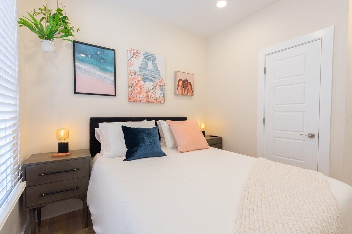 A bedroom with a bed, bedside tables, a nightstand, a door, and wall art.