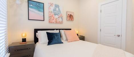A bedroom with a bed, bedside tables, a nightstand, a door, and wall art.